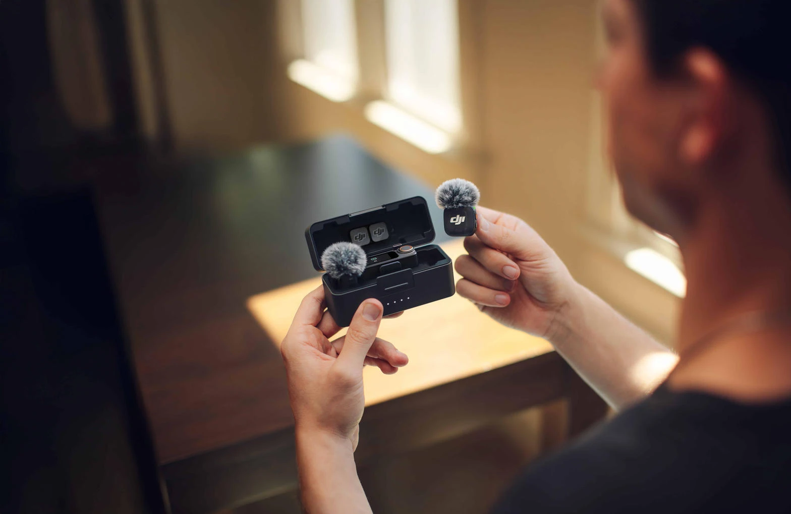 Мужчина держит зарядный кейс DJI Mic и передатчик с ветрозащитой
